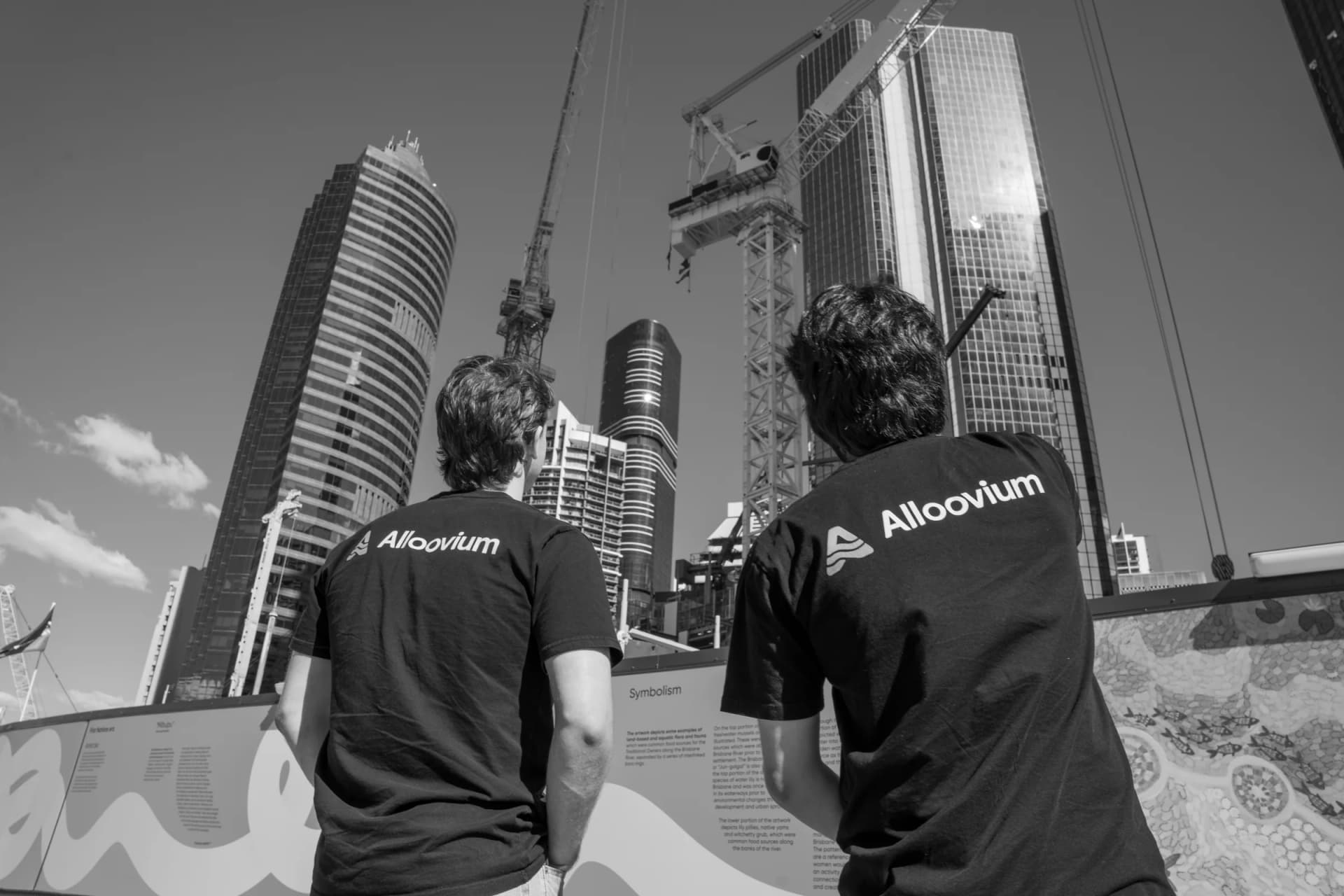 Two Alloovium team members looking toward construction cranes and city buildings